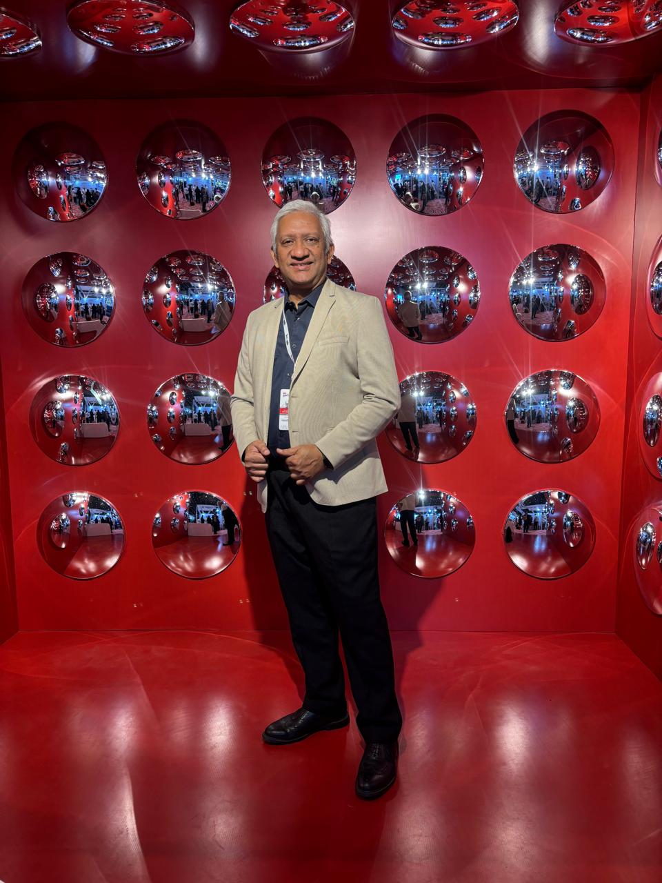 Satish Ramanan at a professional event in front of a red mirrored installation