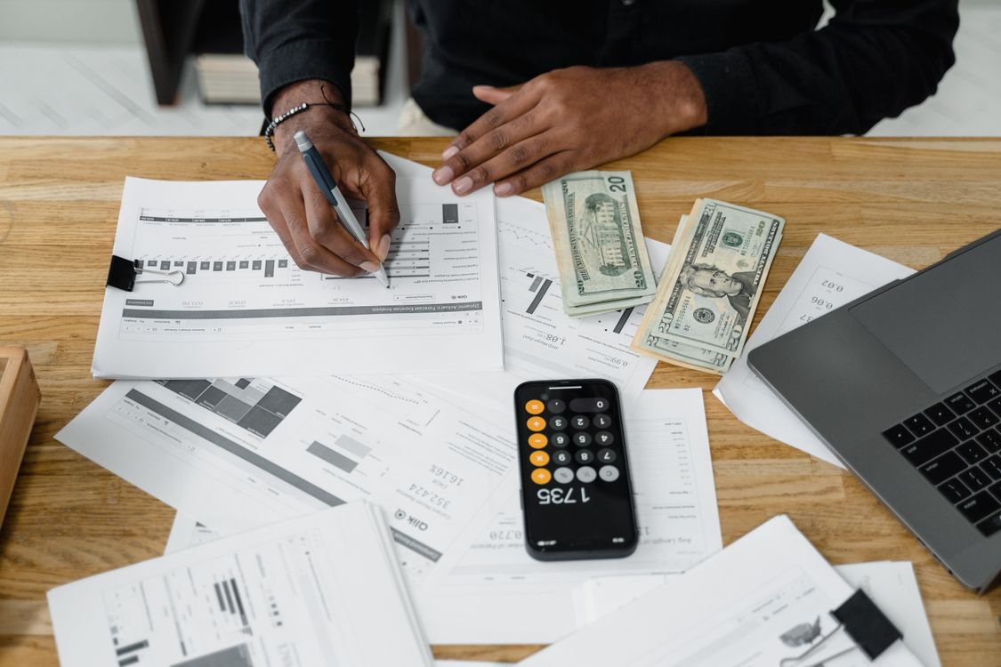 Financial analyst reviewing reports, a calculator, and cash beside a laptop